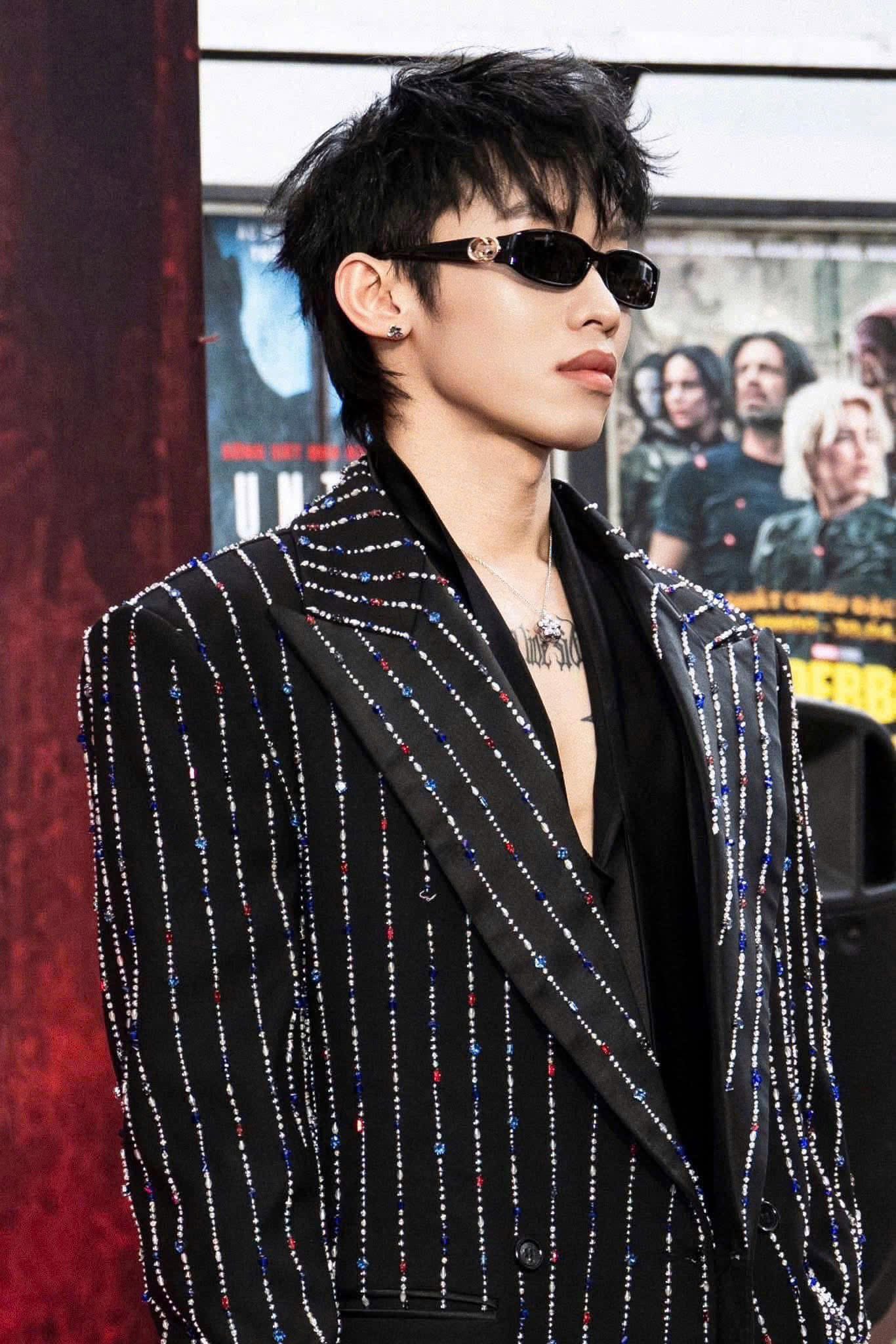 Kay Trần wearing a black and white striped blazer with Gucci GG1661S 001 Sunglasses in front of a movie poster.