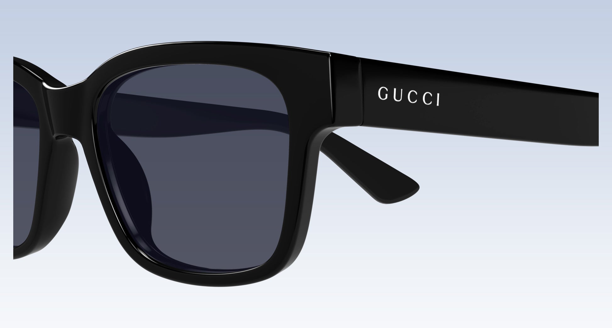 Gucci GG1716S Black Square Sunglasses with a glossy black frame and dark gray lenses, featuring the GUCCI logo printed in white on the temple arm, set against a light blue gradient background.