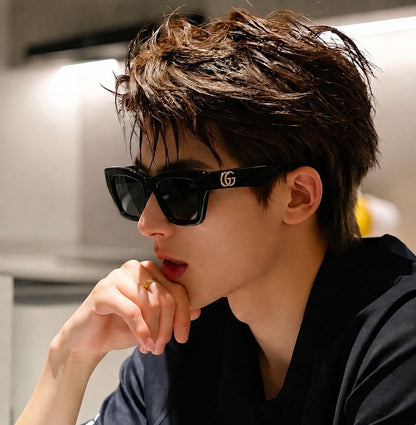 A man wearing black Gucci GG1753S 001 Black Square Sunglasses with the interlocking GG logo on the temple, posing in a modern indoor setting.