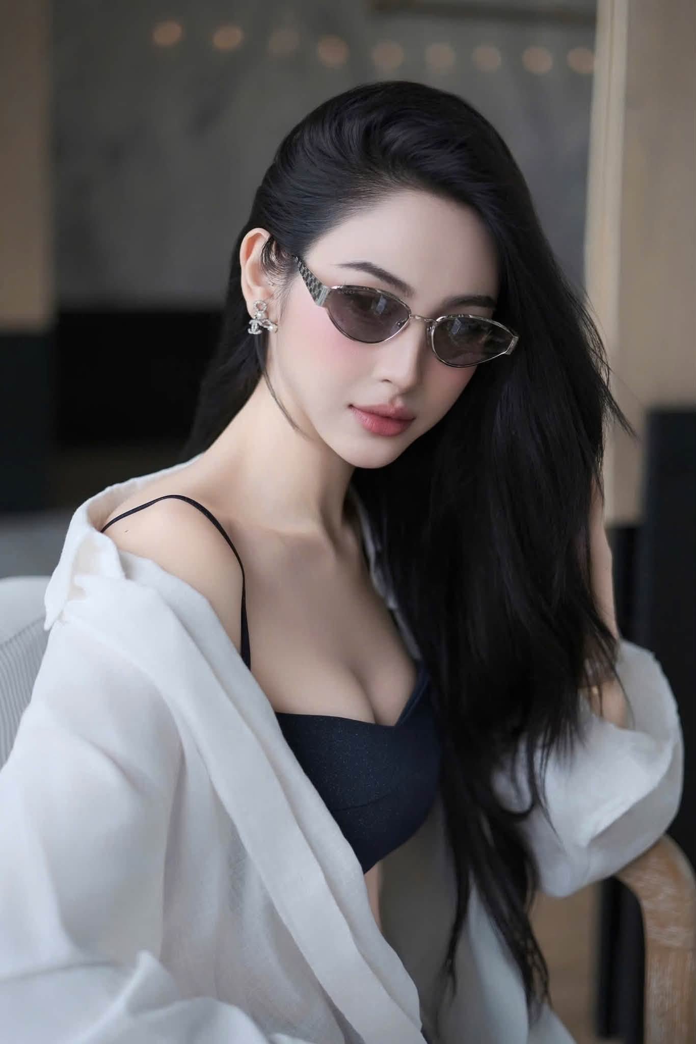 A woman with long black hair wearing Gucci GG1853S 002 Silver Butterfly Sunglasses, a black camisole, and a white open-front shirt, posed indoors against a softly blurred background.