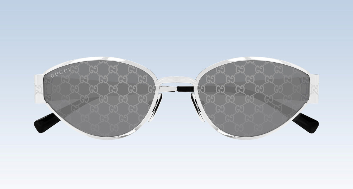 Gucci GG1853S 002 Silver Butterfly Sunglasses with a silver-tone metal frame, featuring the brand's signature GG monogram pattern on the gray lenses and black temple tips, shown against a light blue gradient background.