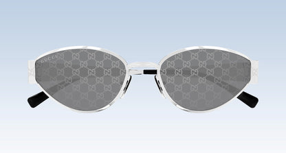 Gucci GG1853S 002 Silver Butterfly Sunglasses with a silver-tone metal frame, featuring the brand's signature GG monogram pattern on the gray lenses and black temple tips, shown against a light blue gradient background.