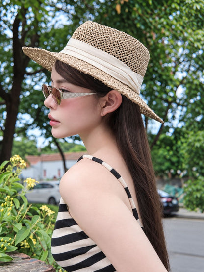 A woman in profile wearing a woven straw boater hat with a cream ribbon band, Gucci GG1853S 003 Gold Butterfly Sunglasses — Brown GG Lens, and a black-and-white striped top, photographed outdoors with trees and a street in the background.