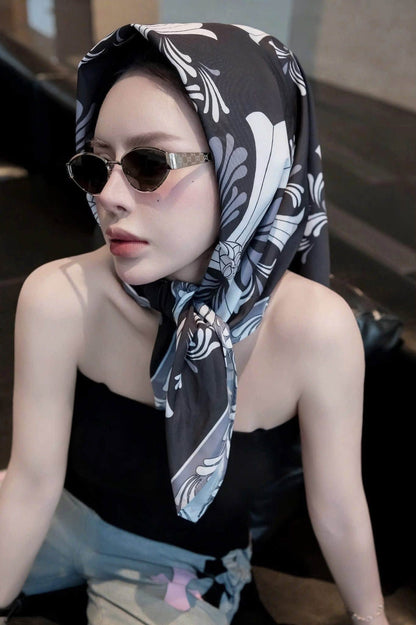 A woman wearing a black, white, and gray patterned headscarf and Gucci GG1853S 001 Gold Butterfly Sunglasses, posing in a dimly lit indoor setting.