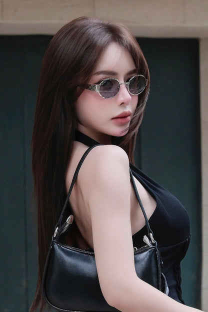 A woman with long dark brown hair wearing round Gucci GG1854S 002 Silver Round Sunglasses, a black halter top, and carrying a black leather shoulder bag, photographed against a dark green door and beige wall background.