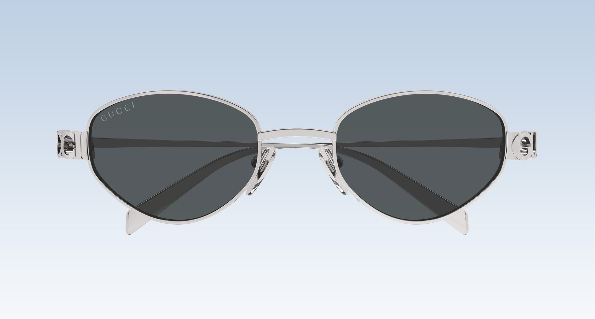 Gucci GG1935S 001 Silver Round Oval Sunglasses with a silver-tone metal frame and dark gray lenses, shown against a light blue gradient background.