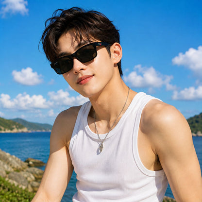 A man outdoors by the sea wearing Gucci GG1986SA 001 Black Rectangular Sunglasses, a white ribbed tank top, and a silver necklace under a bright blue sky with clouds.