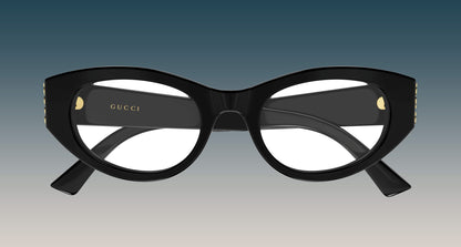 Gucci GG2041O-001 Black Oval Eyeglasses with gold-tone rivets and the Gucci logo printed on the inner temple, shown against a blue-to-gray gradient background.