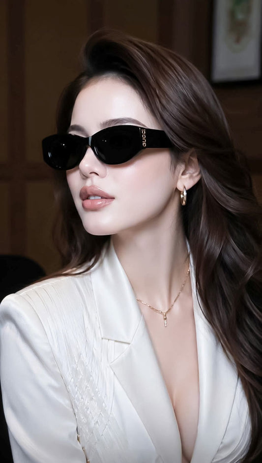 A woman with long brown hair wearing Gucci GG2044SA-001 Black Soft Rectangular Sunglasses with gold lettering on the temple, a white blazer, and gold jewelry, photographed in a warm indoor setting.