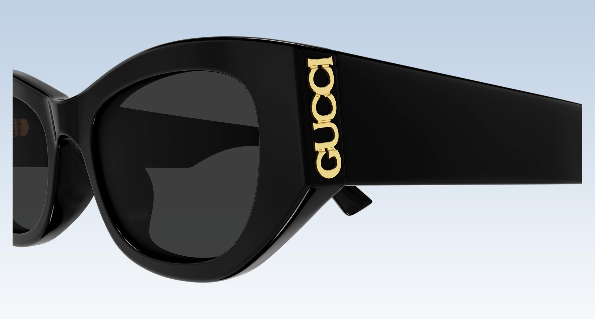 Close-up of Gucci GG2044SA-001 Black Soft Rectangular Sunglasses with dark lenses and a gold-tone vertical GUCCI logo on the temple, shown against a light blue gradient background.