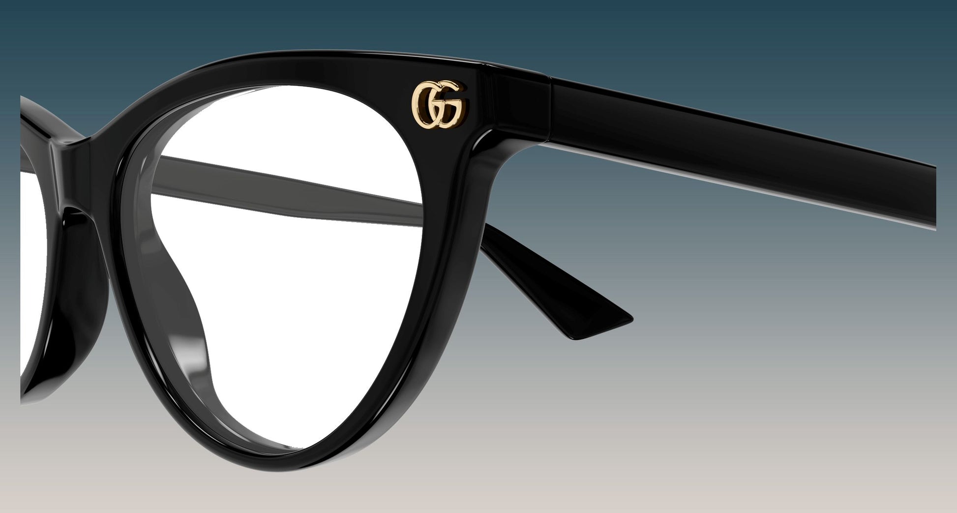 Close-up of a pair ofGucci GG2112O-001 Black Butterfly Eyeglasses with a gold interlocking G logo on the upper frame, set against a gradient blue-to-gray background.