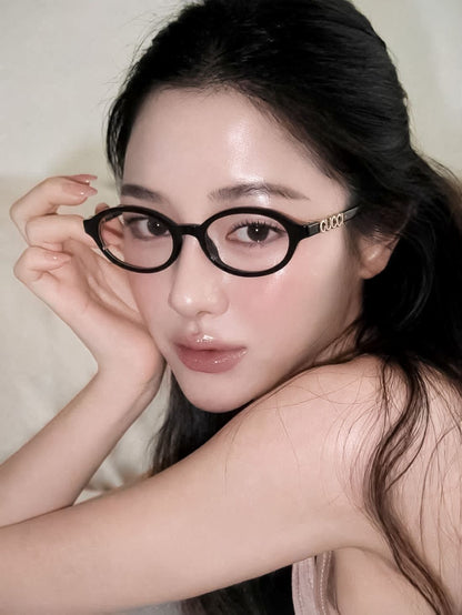 A close-up portrait of a woman wearing Gucci GG2153O Round Eyeglasses with gold-tone 'Gucci' lettering on the temple, posed against a soft beige background.