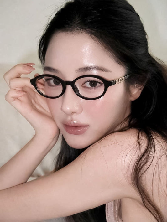 A close-up portrait of a woman wearing Gucci GG2153O Round Eyeglasses with gold-tone 'Gucci' lettering on the temple, posed against a soft beige background.