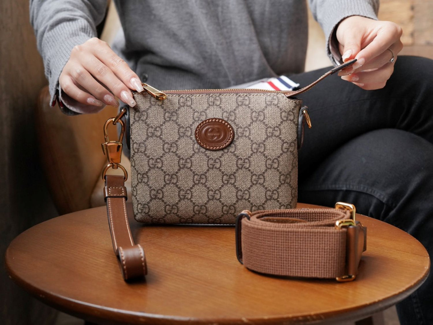 Person holding a Gucci Interlocking G Mini Messenger Bag Beige 723306 92THG 8563 with a strap on a wooden table