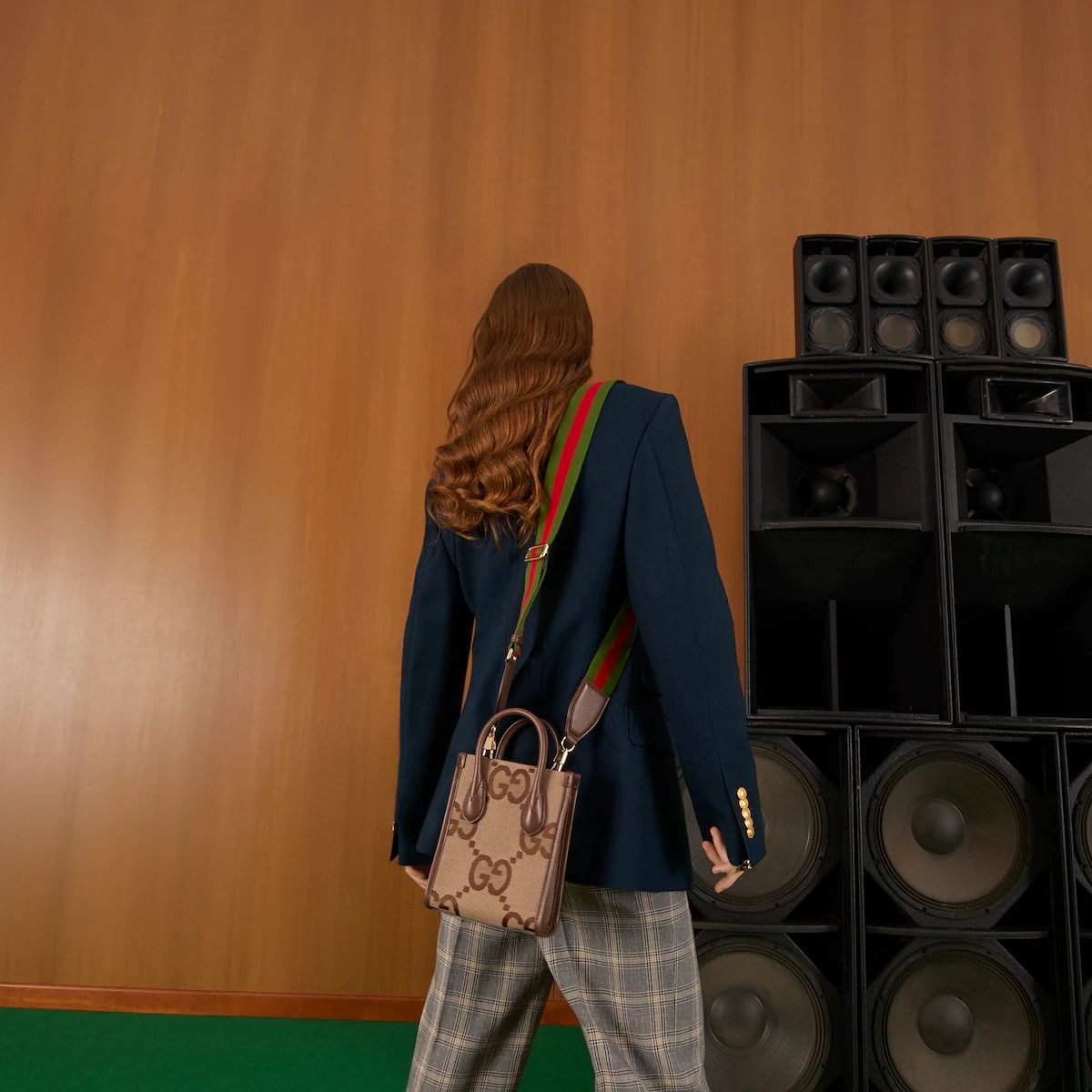 Person in a blue blazer with a Gucci Jumbo GG Mini Tote Bag Camel Ebony 699406 UKMDG 2570 standing in front of audio equipment.