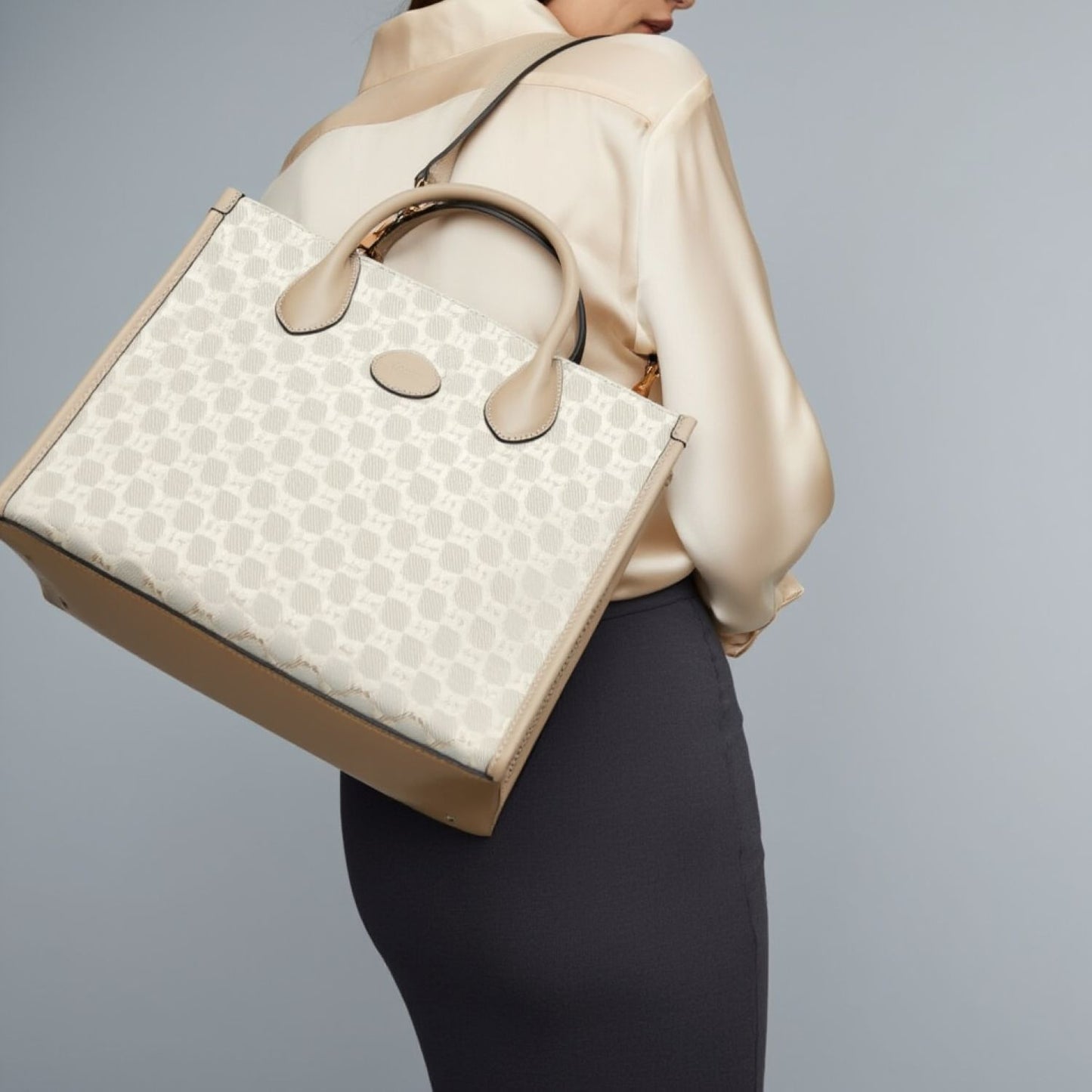 Person wearing a Gucci Small Tote Bag With Interlocking G Beige 659983 UULBT 9683 against a gray background
