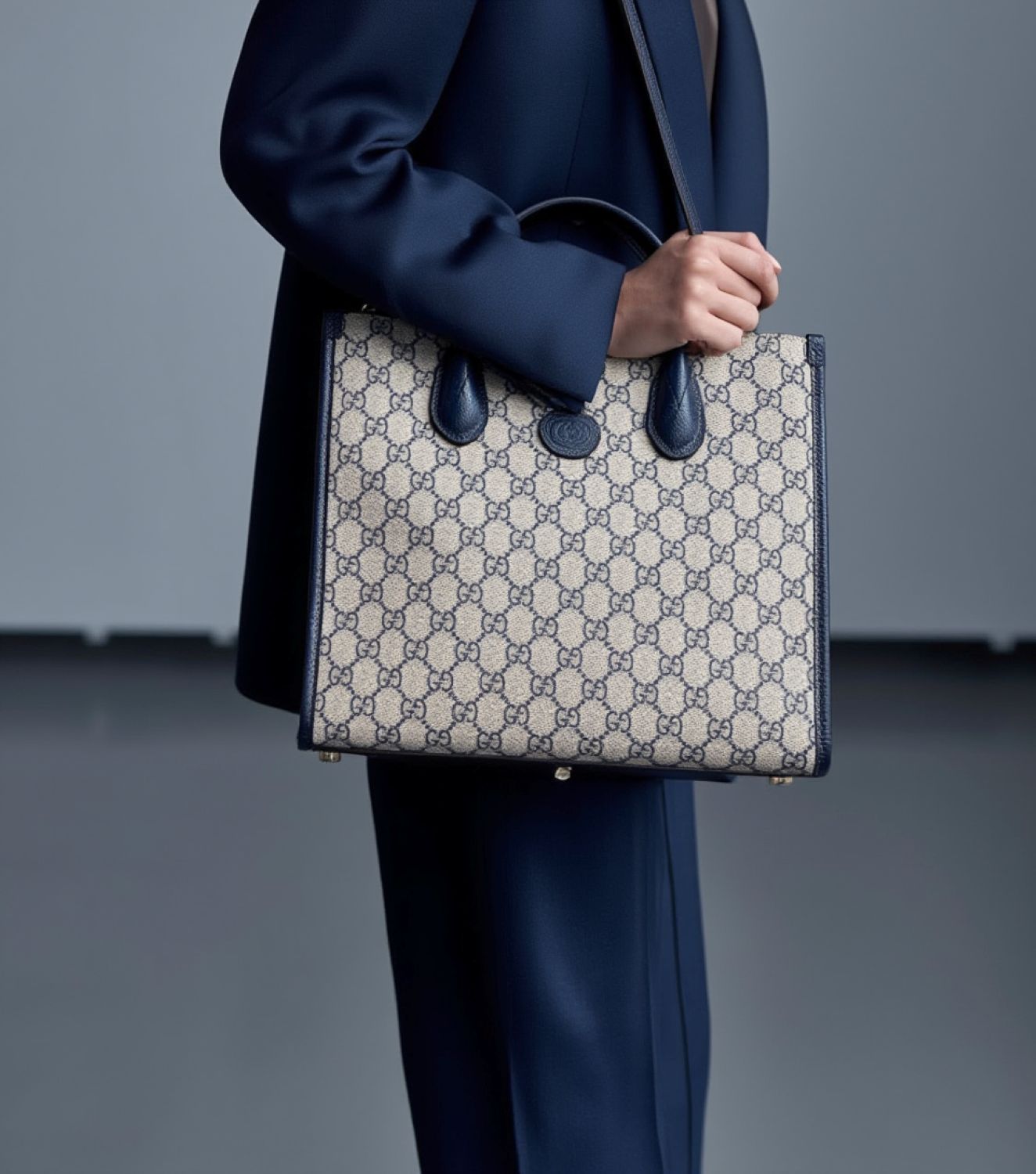 Person holding a Gucci Small Tote Bag With Interlocking G Navy 659983 K9GSN 4075 against a plain background