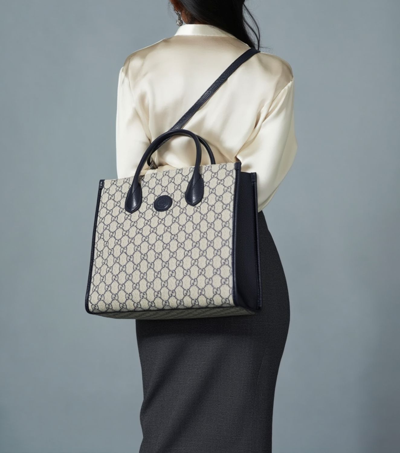 Person holding a Gucci Small Tote Bag With Interlocking G Navy 659983 K9GSN 4075 a gray background