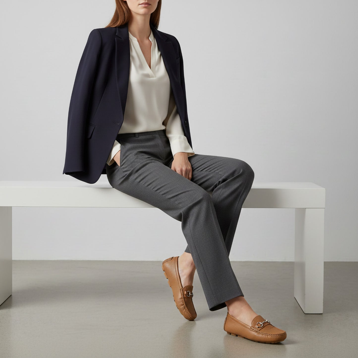 Person sitting on a white bench wearing a navy blazer, white shirt, gray pants, and Gucci Women’s Horsebit Driver Loafers Brown 815464 AAC4Q 2712.