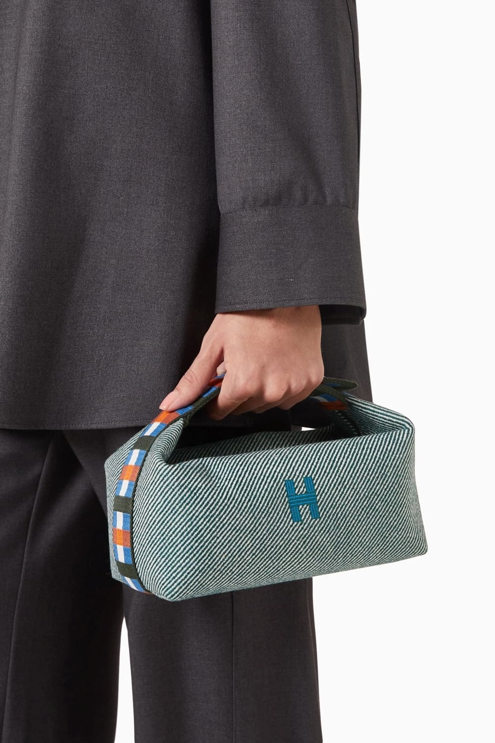 Person holding a Hermès Small Bride-à-Brac au Carré Toiletry Bag Green Forest H103802Mv03 with a logo, wearing a dark gray coat and pants.