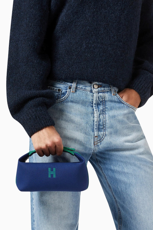 Person holding a Hermès Small Bride-a-Brac Case Marine H103222Mv03 with a green handle and logo, wearing a dark sweater and light blue jeans.