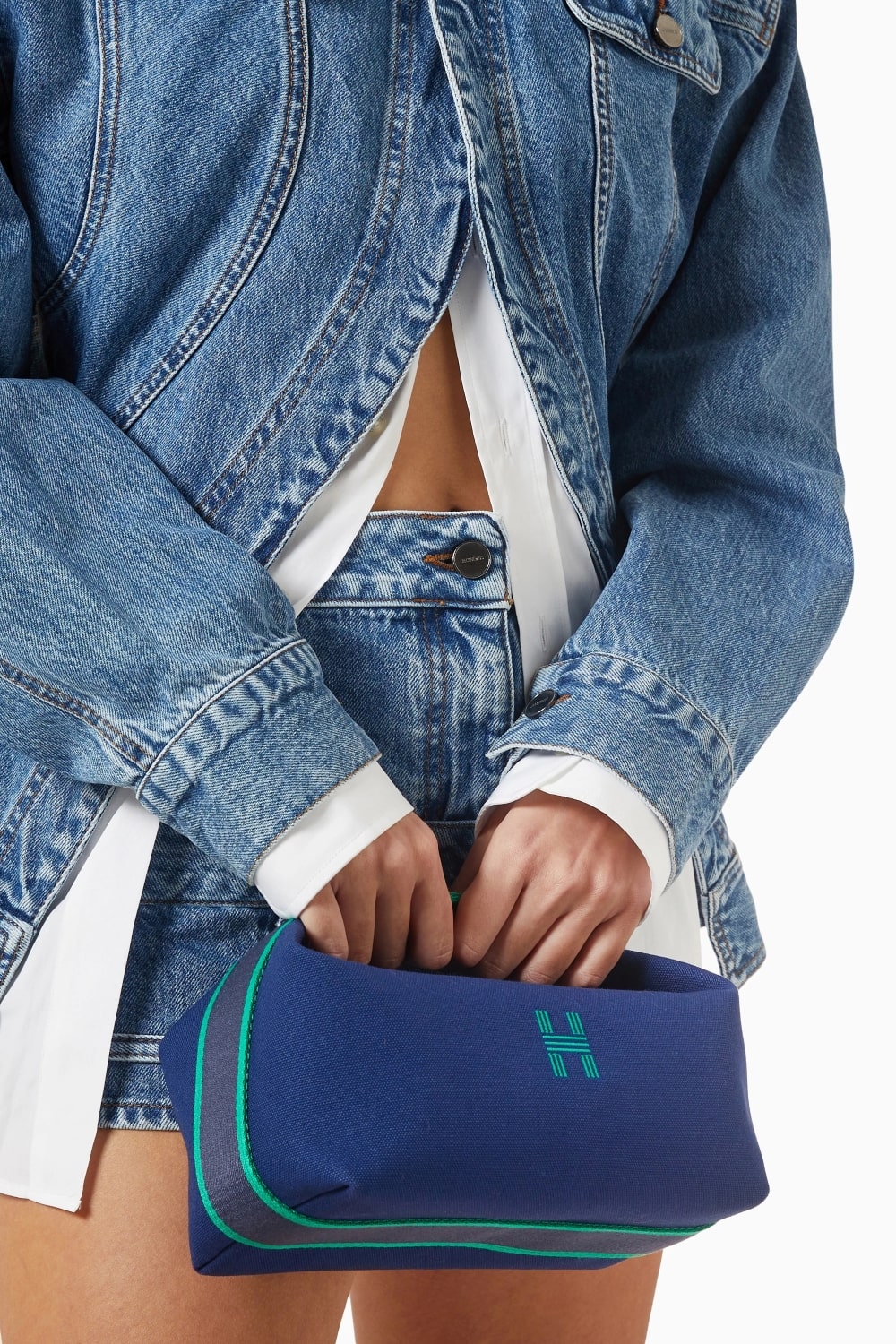 Women holding a Hermès Small Bride-a-Brac Case Marine H103222Mv03 with a logo, wearing a denim jacket and skirt.