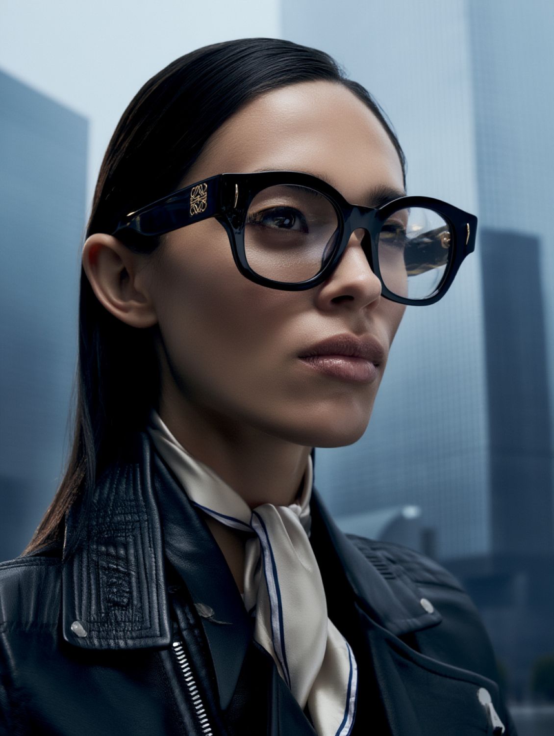 women wearing Loewe LW50096I 001 Anagram Round-Square Black Eyeglassess with a blurred cityscape background