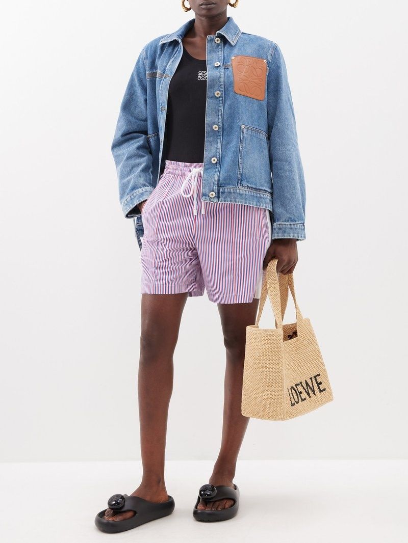 Model wearing a Loewe Paula Ibiza Foam Thong Slide Black L616S03X02 1100, holding a straw bag with 'LOEWE' branding.