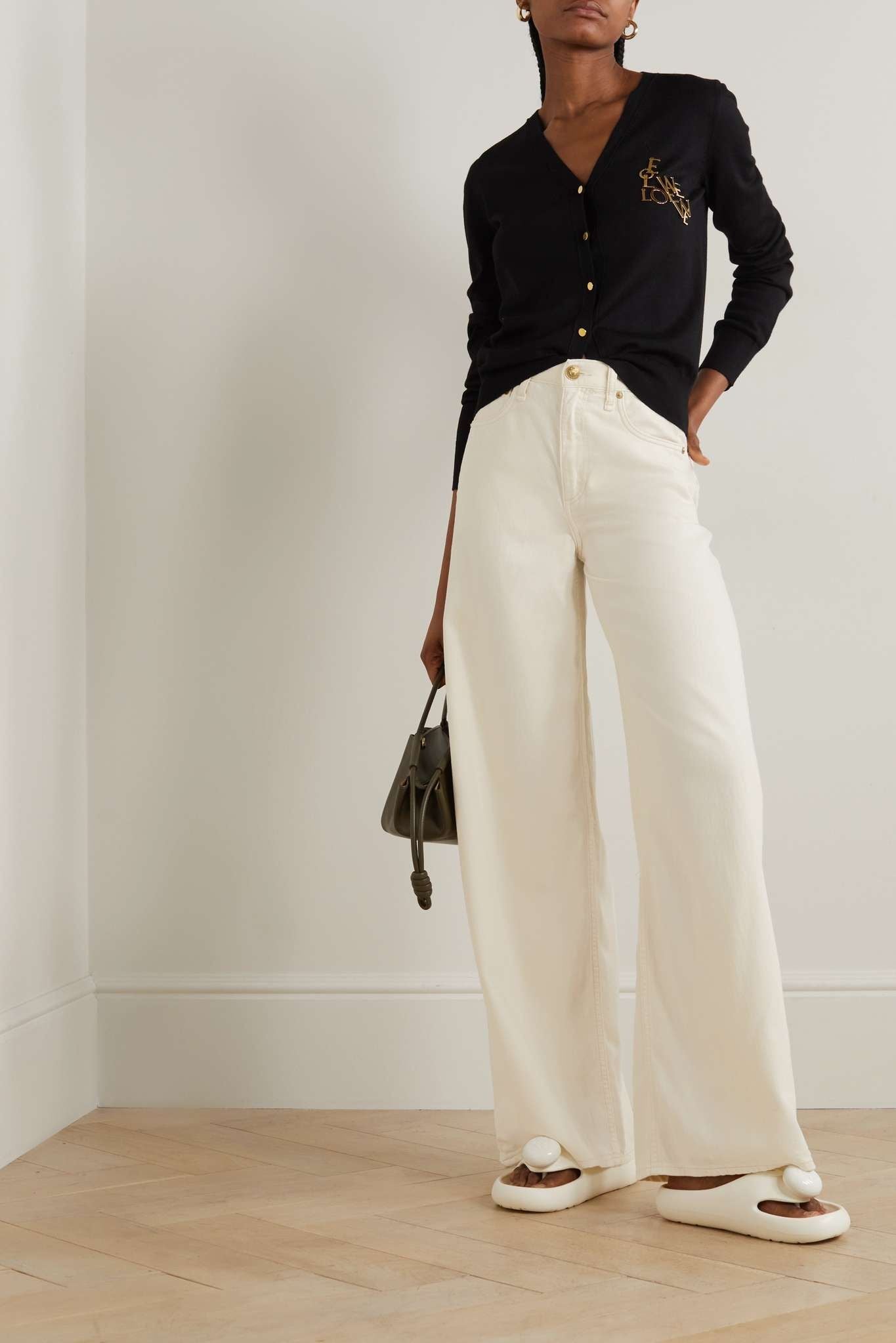 Women wearing a black cardigan and white pants with Loewe Paula Ibiza Foam Thong Slide White L616S03X02 2100 standing against a plain background