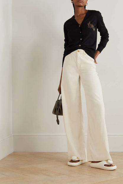 Women wearing a black cardigan and white pants with Loewe Paula Ibiza Foam Thong Slide White L616S03X02 2100 standing against a plain background