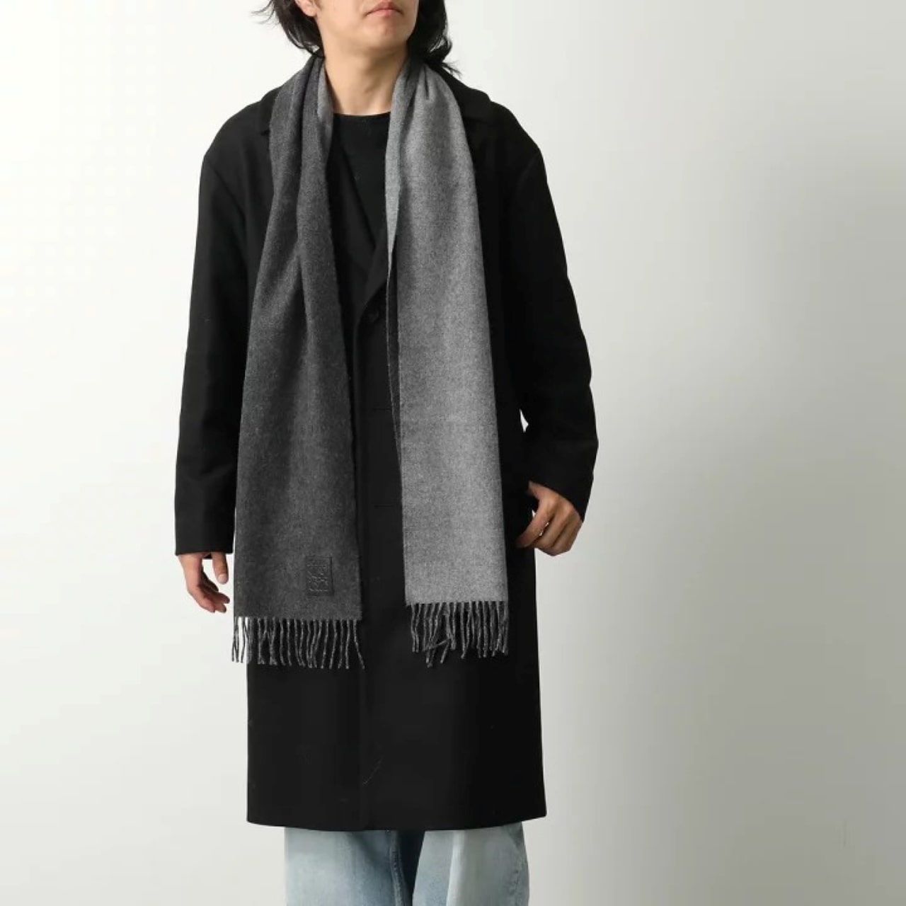 Person wearing a long black coat and Loewe Scarf in Wool and Cashmere Black/Grey F811251X06-1114 on a white background