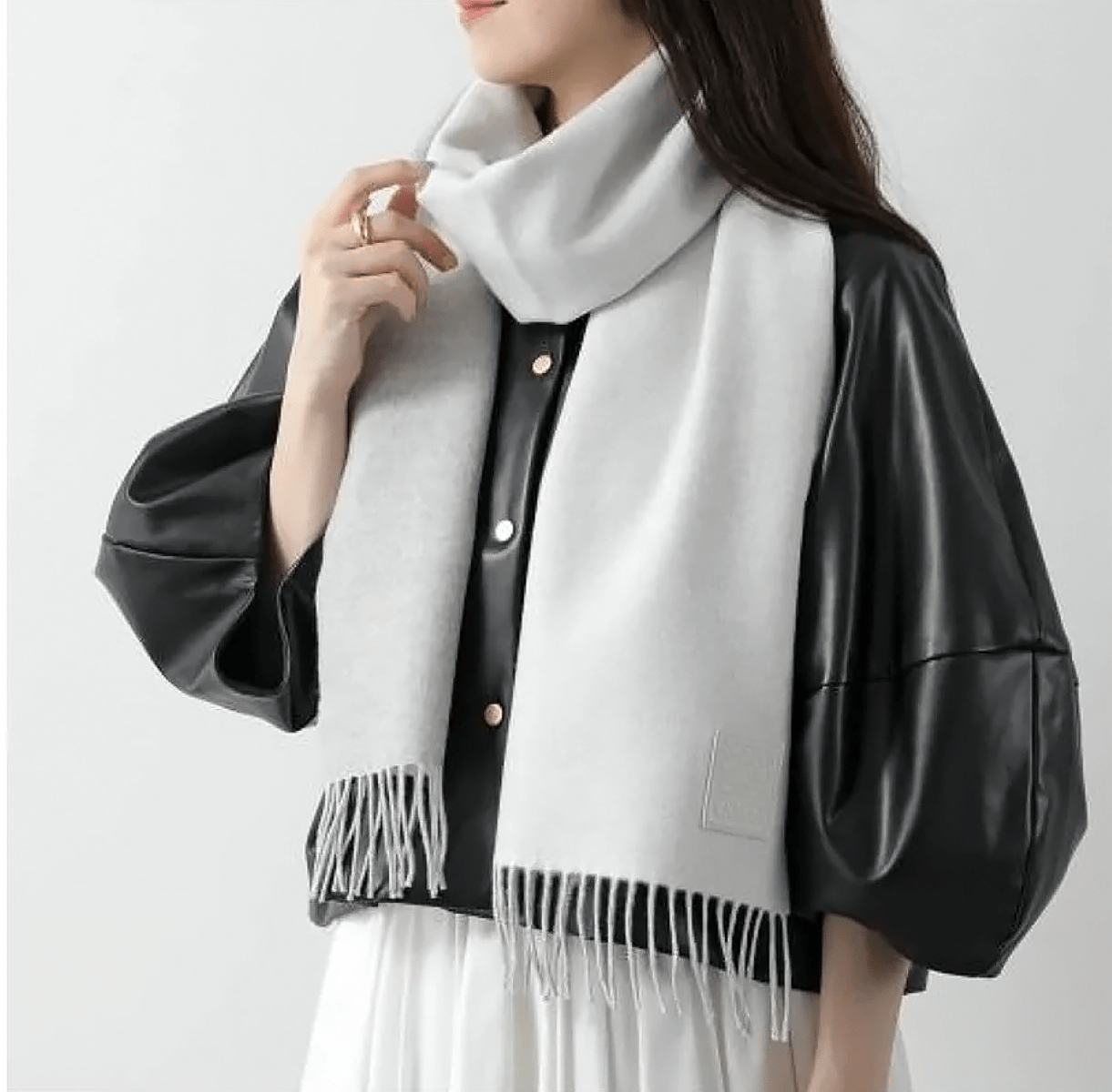 Person wearing aLoewe Scarf in Wool and Cashmere White/Light Grey F811251X06-2013 with black leather jacket and white dress on a light gray background