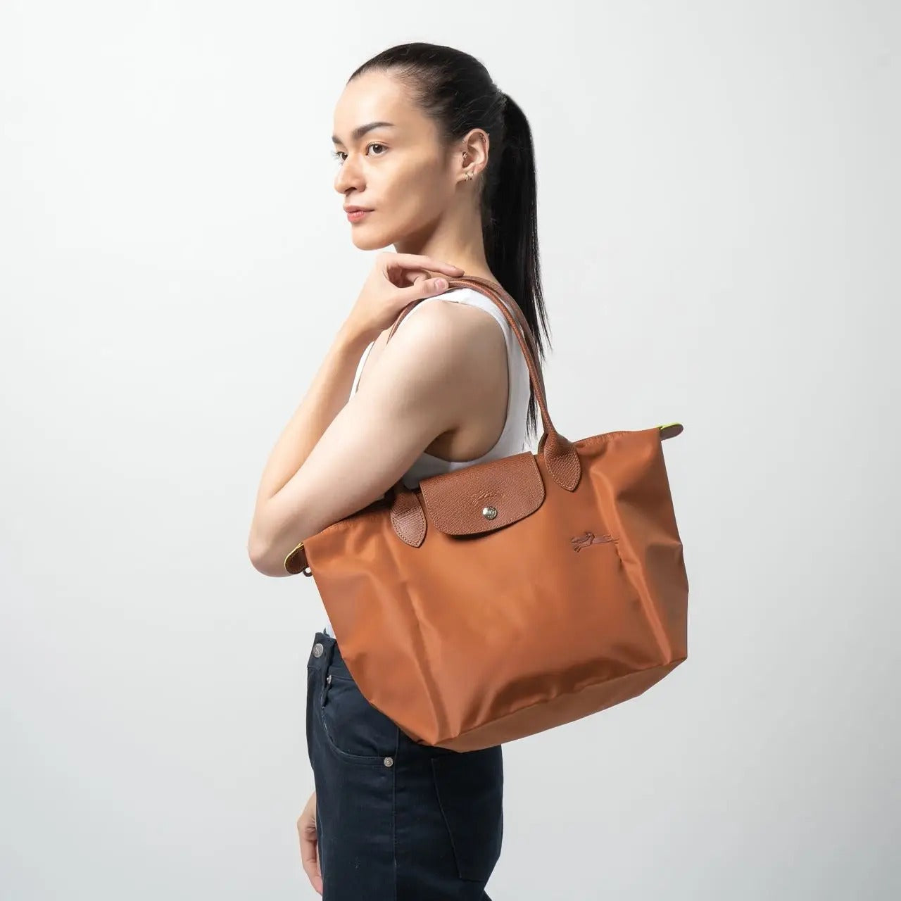 Woman carrying a Longchamp Le Pliage Green M Tote Bag – Cognac L2605919504 on a plain background