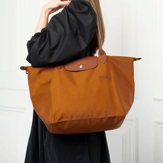 Person holding a Longchamp Le Pliage Original L Tote Bag – Cognac L1899089504 with a brand logo against a white background