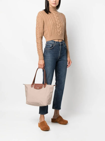 Woman holding a Longchamp Le Pliage Original M Tote Bag – Pebble L2605089349 wearing a beige sweater, blue jeans, and brown shoes on a white background