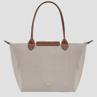 behind Longchamp Le Pliage Original M Tote Bag – Pebble L2605089349 with brown handles on a light gray background
