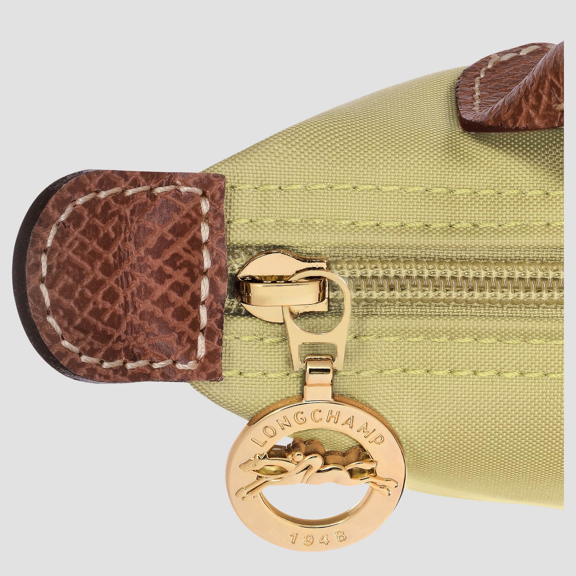 Close-up of a gold Longchamp charm on a green bag with brown leather accents.