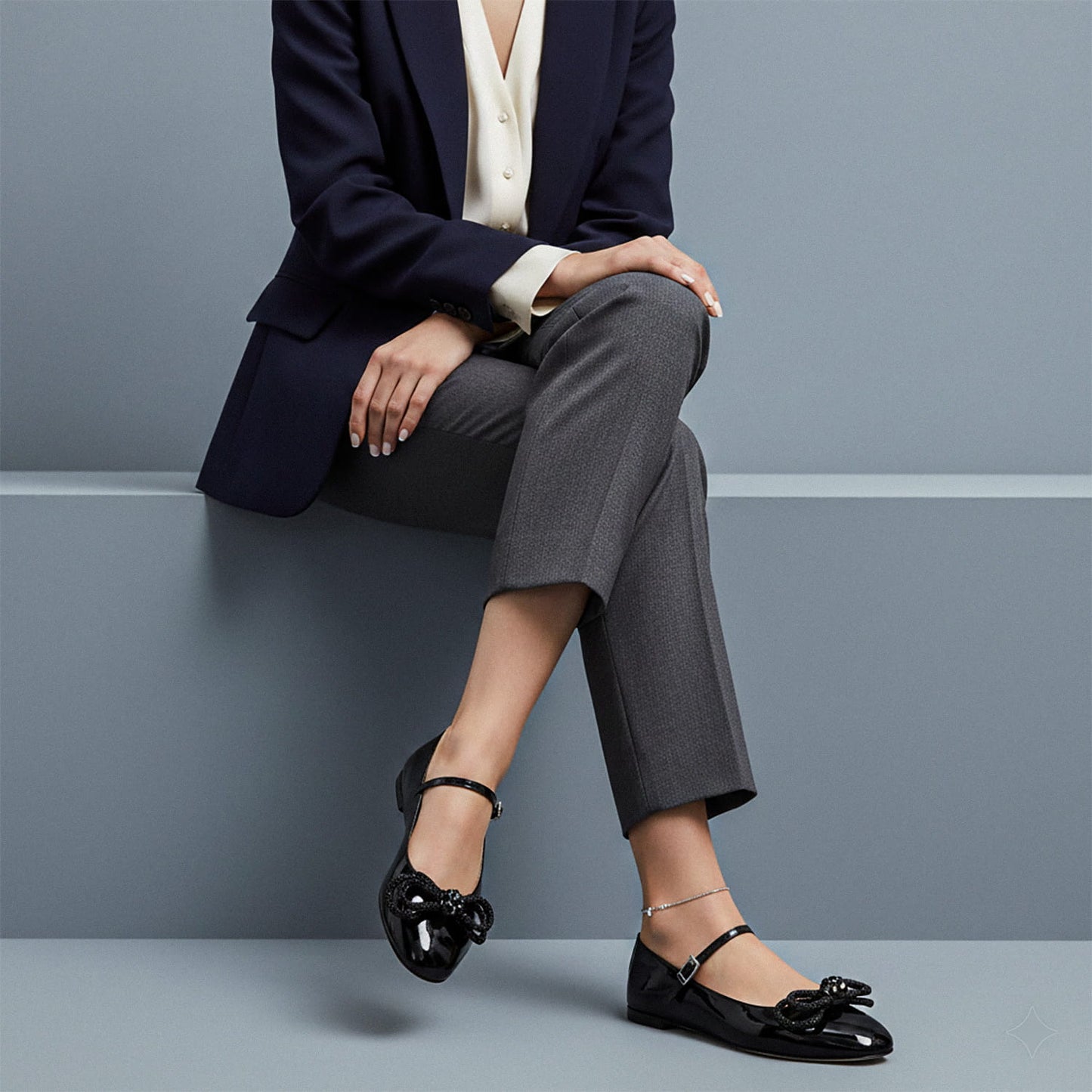 Person wearing a navy blazer, gray pants, and MACH & MACH Double Bow Black Patent Ballet Flat sitting on a gray surface.