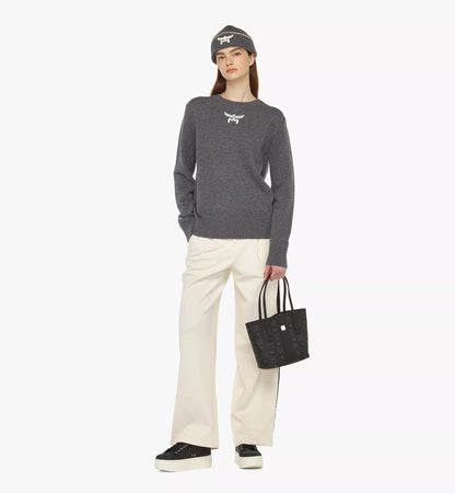 Person wearing a gray sweater, white pants, black shoes, and a MCM Mini Reversible Liz Shopper in Visetos Black MWPDALR01BK001 on a white background