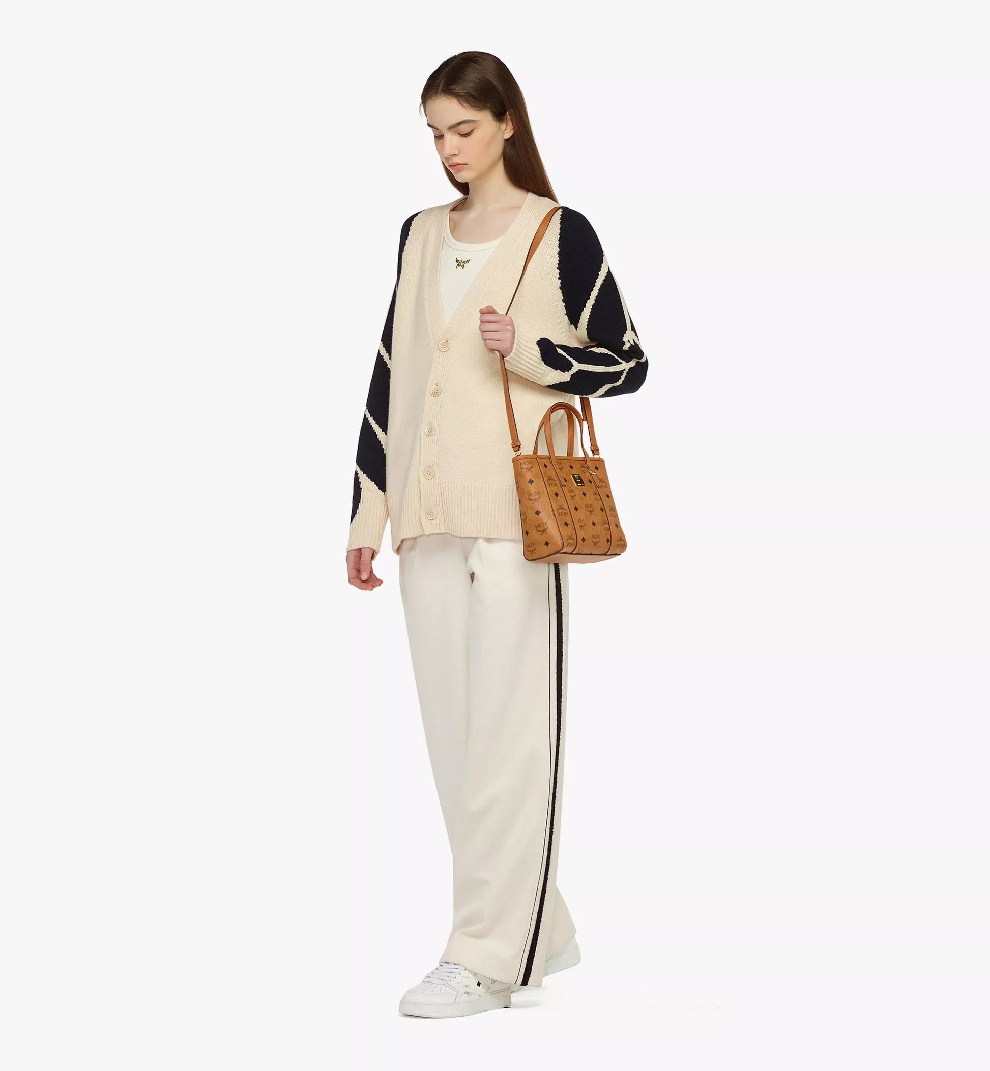 Woman wearing a black, white, and beige outfit with a MCM Mini Toni Top-Zip Shopper in Visetos Cognac MWPAATN04CO001 on a white background