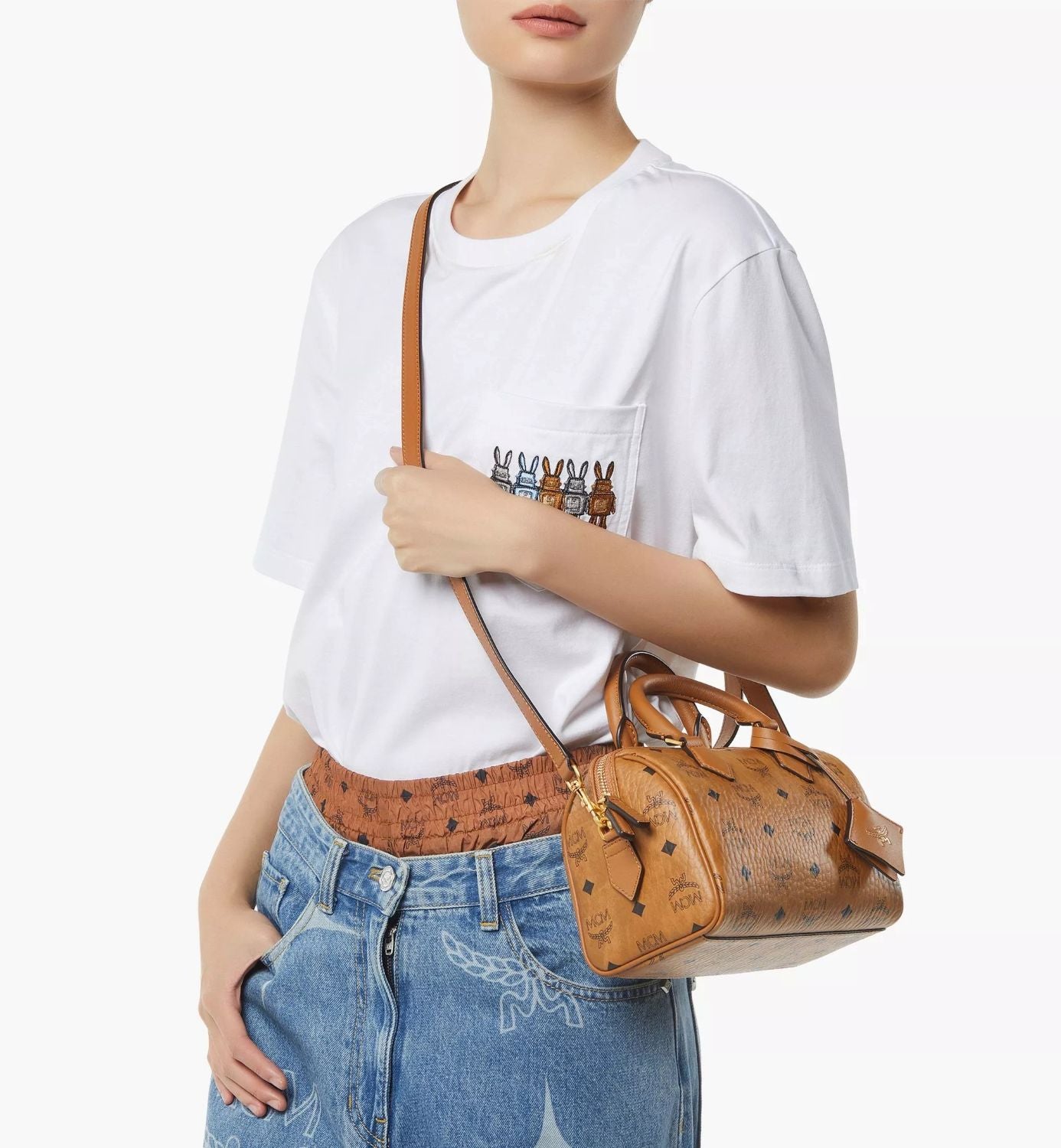 Person holding a MCM Small Ella Boston Bag in Visetos Cognac MWBFAEA03CO001 with a white t-shirt and blue jeans.