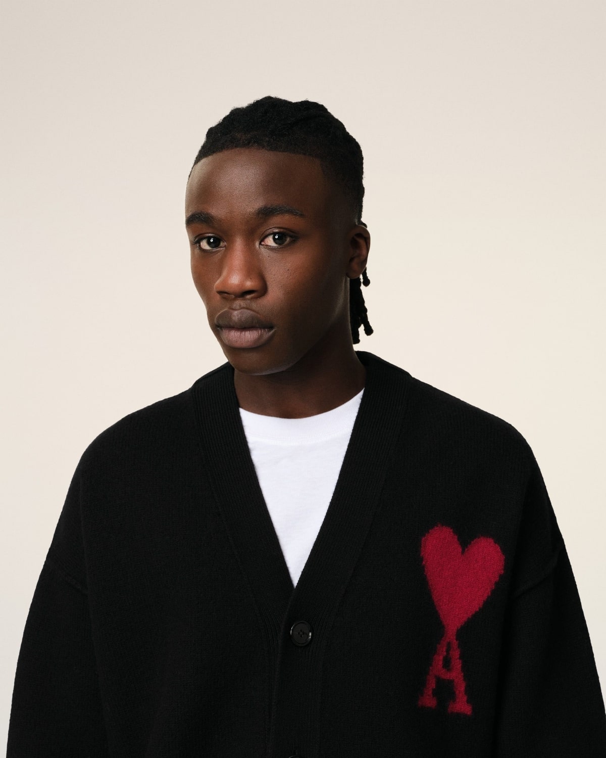 Person wearing a Merino Wool Ami De Coeur Cardigan Black/Red BFUKC006.018.009 with a red heart and letter 'A' design on a beige background