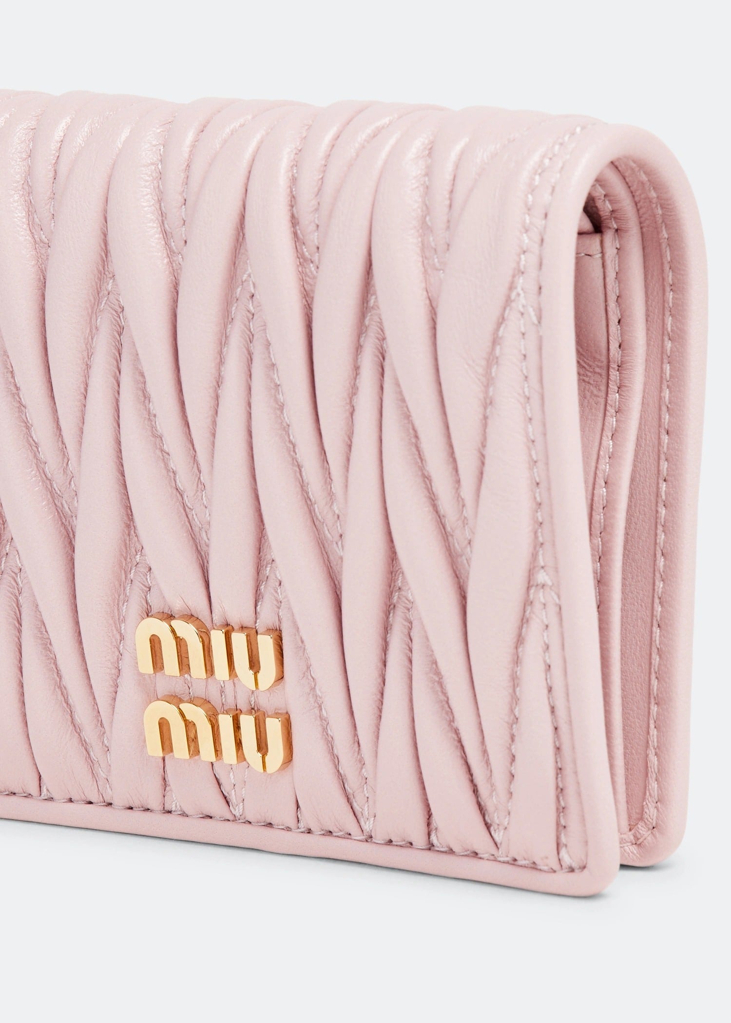 Pink quilted wallet with gold 'miu miu' logo on a light gray background