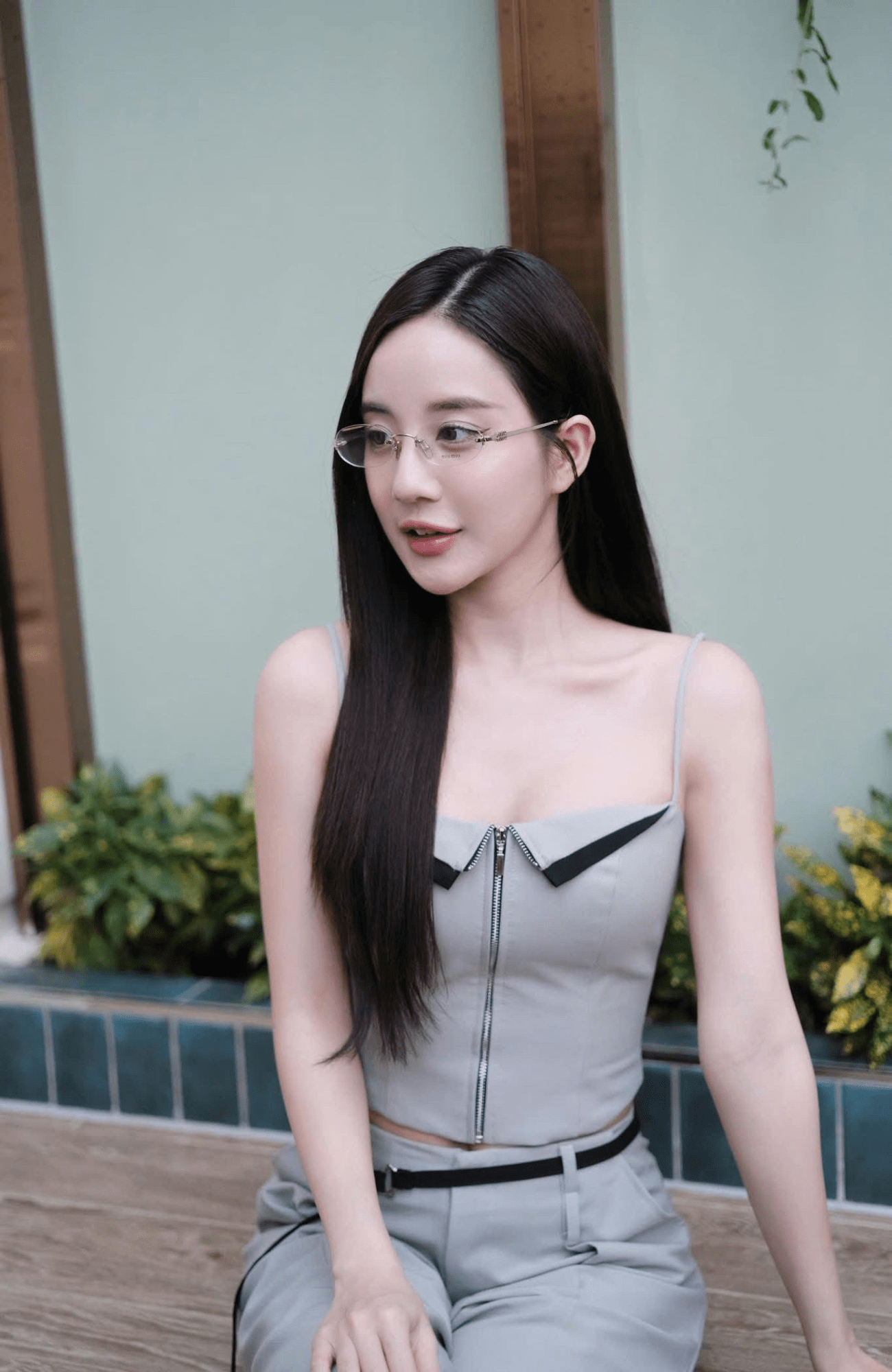 Woman wearing Miu Miu MU 53WV 1BC1O1 Eyeglasses and a gray outfit sitting outdoors with plants in the background