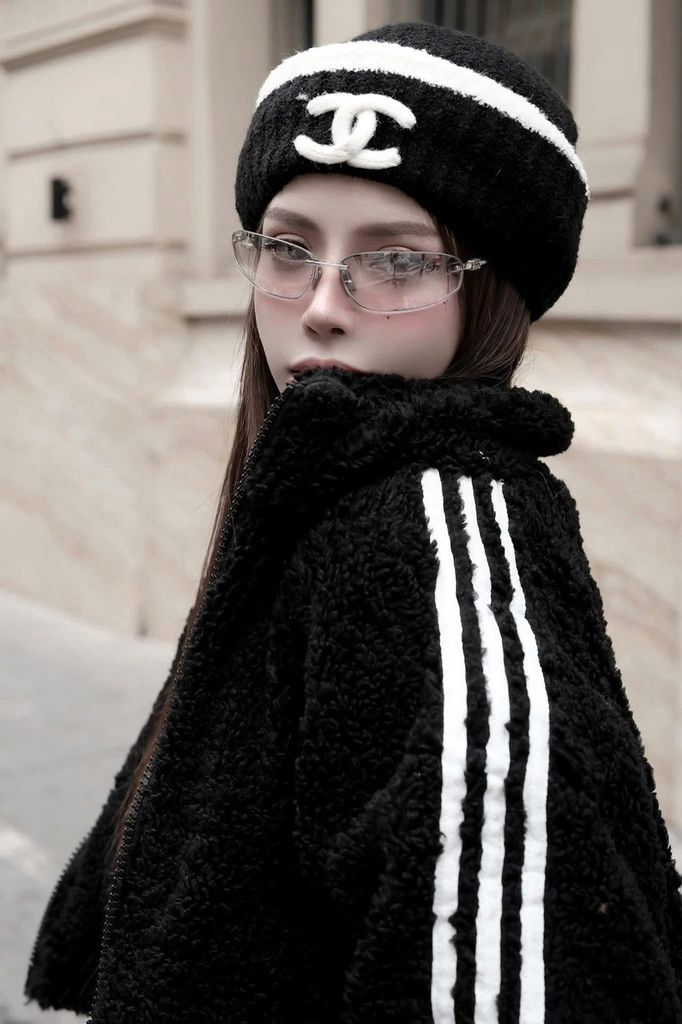 Person wearing Miu Miu MU A50S 1BC8H1 Sunglasses and a black coat with white stripes and a Chanel beanie outdoors.