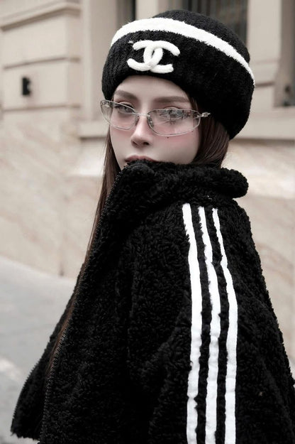 Person wearing Miu Miu MU A50S 1BC8H1 Sunglasses and a black coat with white stripes and a Chanel beanie outdoors.