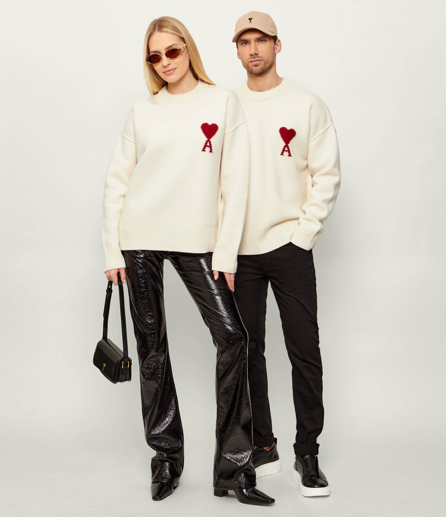 Two people wearing Ami Paris Natural Wool Crewneck Sweater With Contrasted Ami De Coeur Off/White UKS838.018.154 with red heart designs on a plain background