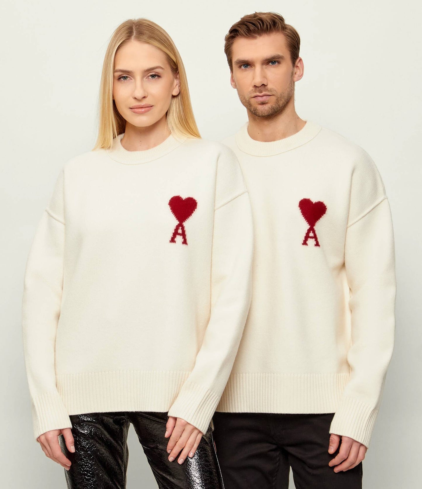 Two people wearing Ami Paris Natural Wool Crewneck Sweater With Contrasted Ami De Coeur Off/White UKS838.018.154 with red heart designs on a plain background