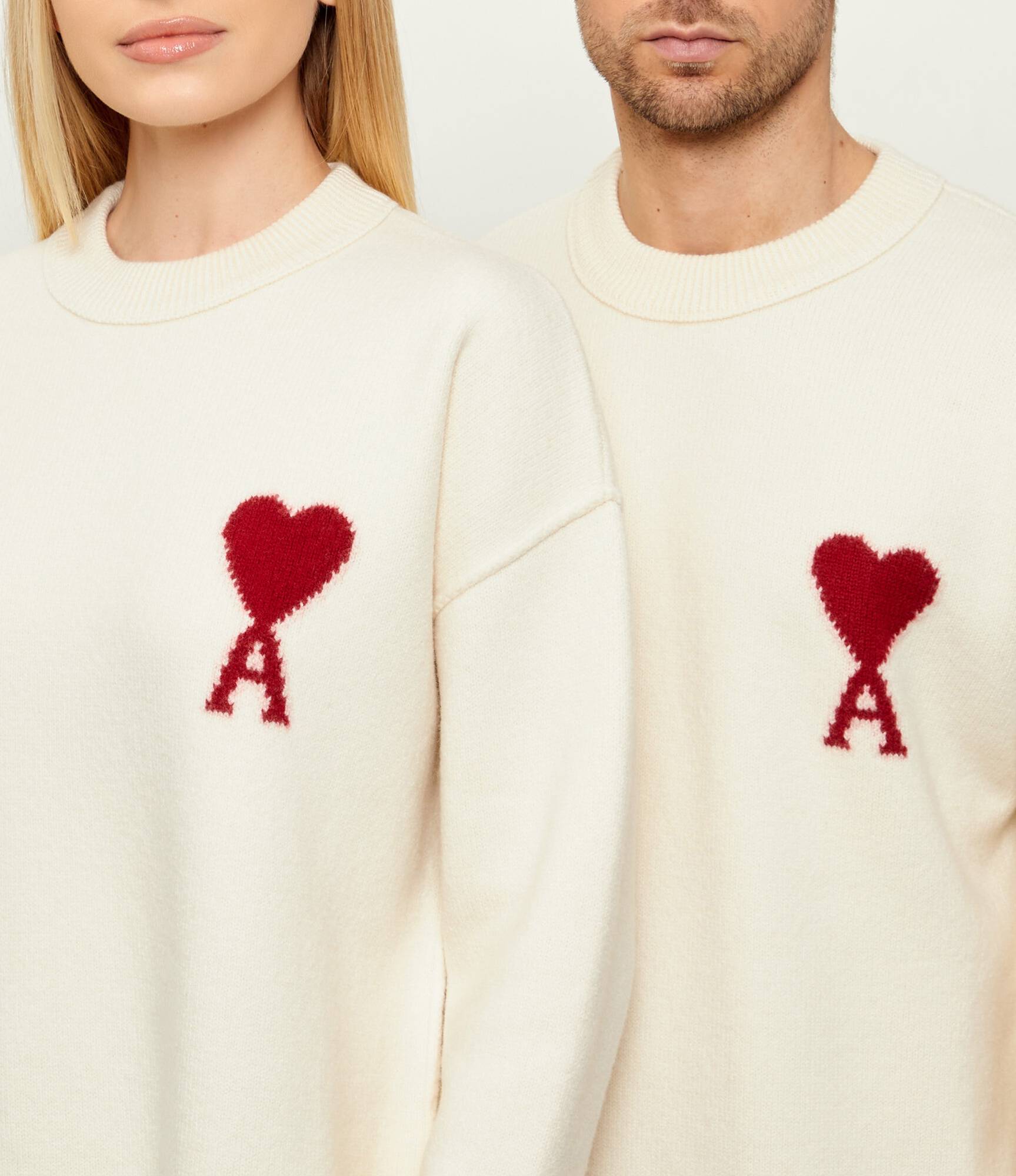 Close-up two people wearing Ami Paris Natural Wool Crewneck Sweater With Contrasted Ami De Coeur Off/White UKS838.018.154 with red heart designs.