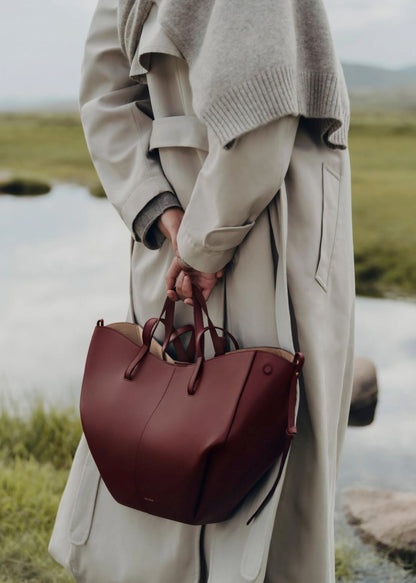 Person holding a mPolène Cyme Edition Textured Black Cherry in a natural setting with water and greenery.